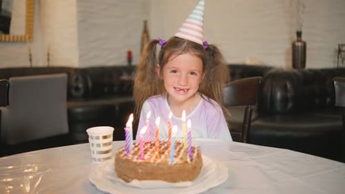 Uma jovem comemora seu aniversário com um bolo e velas coloridas usando um chapéu de festa e