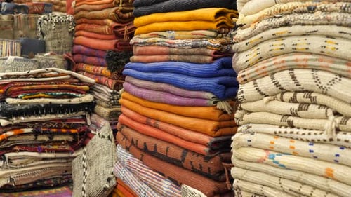 A set of handmade carpets and textiles stacked inside a Moroccan store.