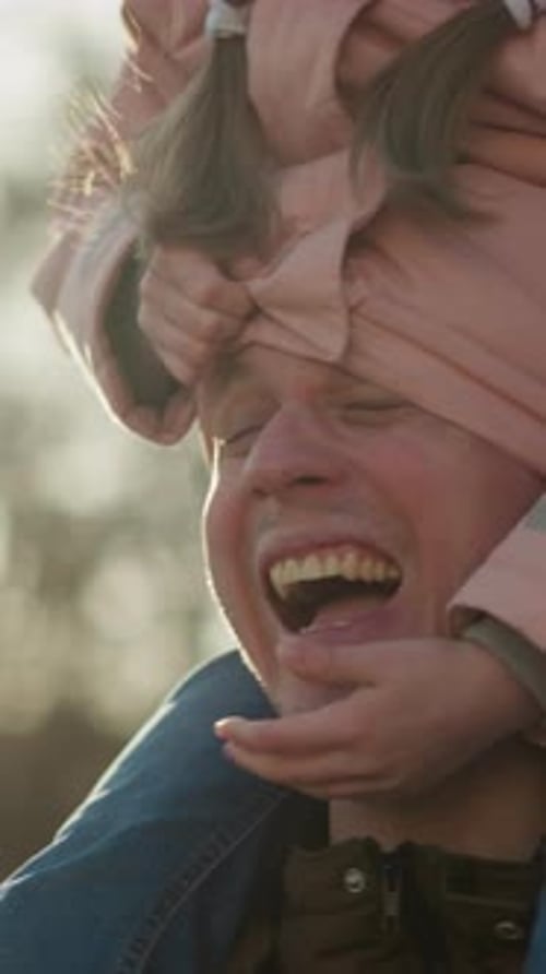 Joyful Girl in Pink Jacket and Cap Playing with Dad Outdoors