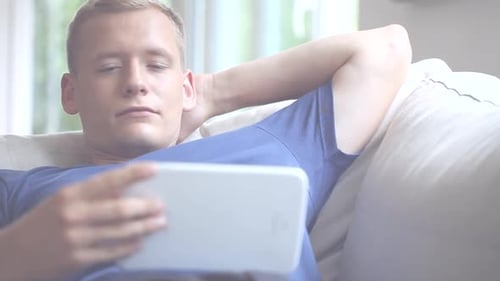Smiling Man Relaxing on Sofa Using Tablet Device