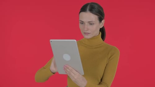 Woman Smiles While Using Tablet on Red Backdrop