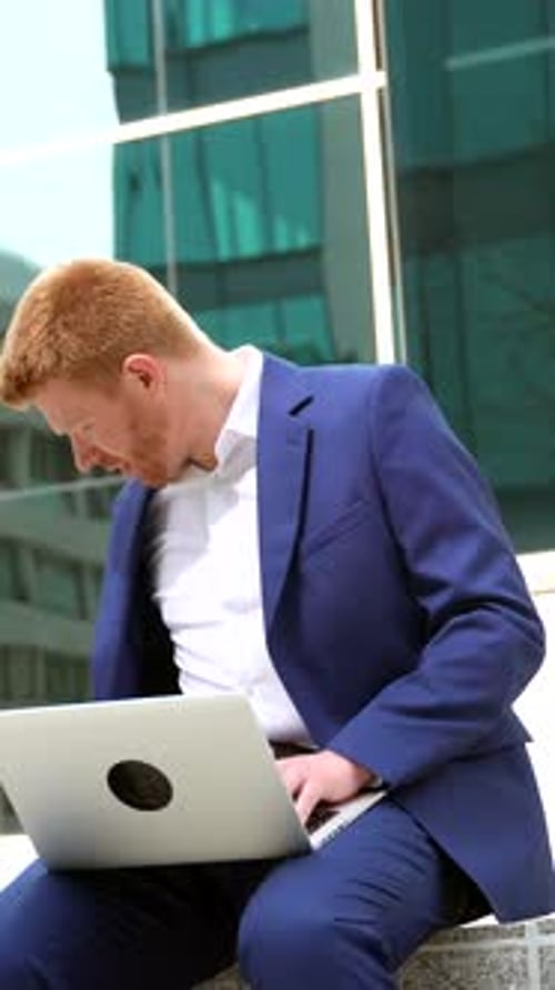 Businessman Talking to the Mobile While Working with Laptop in the City