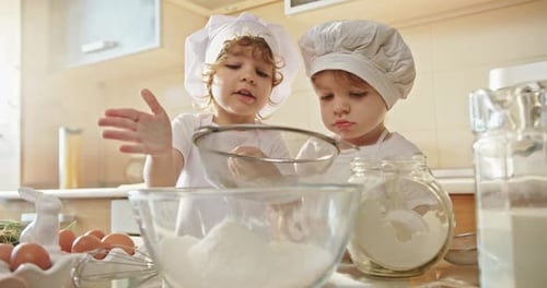 Dos niños con sombreros de chef divirtiéndose mezclando harina en un tazón
