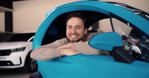 Smiling Man Sits Inside of His New Auto Male Made Purchase in Car Showroom