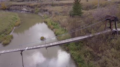 Battered and neglected old suspension bridge over tiny badlands river