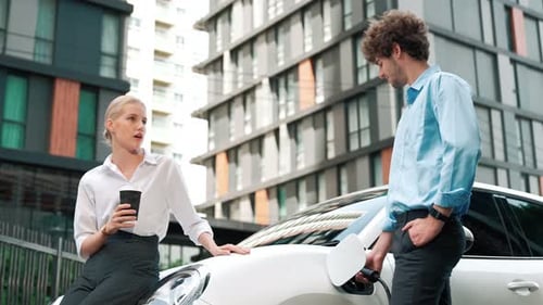 Progressive businessman and businesswoman leaning on EV car and charging point.