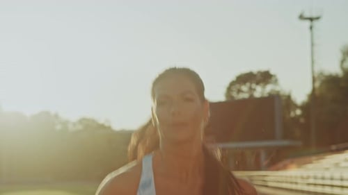 Beautiful Fitness Woman in Light Blue Athletic Top Jogging in an Outdoors Stadium. She is Running o