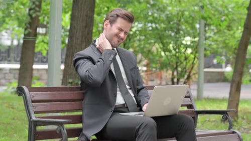 Businessman Massaging Neck While Working on Laptop in Park