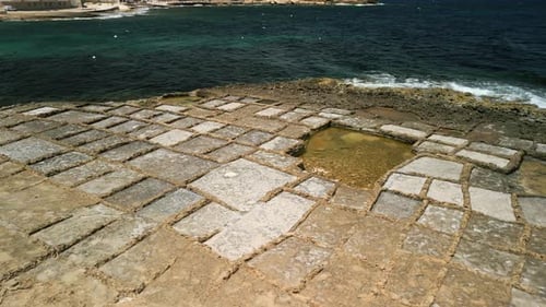 Rotating aerial footage of rectangular salt pans with sea waves on the coast of Gozo, Malta