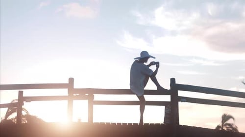 Independent woman captures tropical sunset with smartphone on resort pier