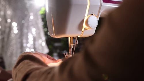 Woman sewing fabric with professional machine in workshop, closeup