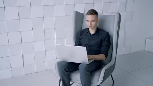 Man Typing on Laptop in Modern Chair