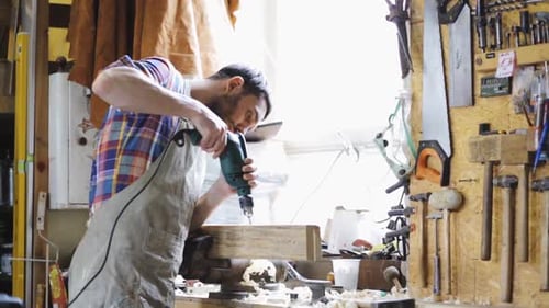 Man drills wood in workshop with power tool