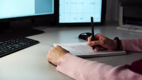 Close Up Hands of Businesswoman Holding Pen and Papers Making Notes in Notepad on Table