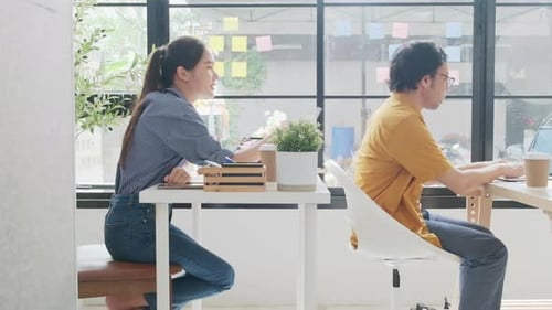 Two young Asian startup partners are working in a casual small business office.