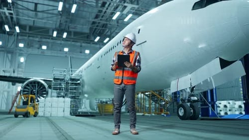 Asian Male Engineer Looking At The Tablet And Looking Around While Aircraft Maintenance