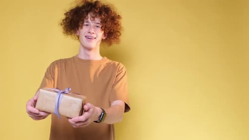 Curly Man with a Christmas Present in His Hands on a Yellow Background in the Studio