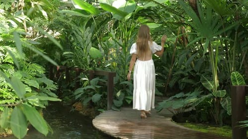 Woman Walking on Wooden Pathway in Tropical Garden Surrounded By