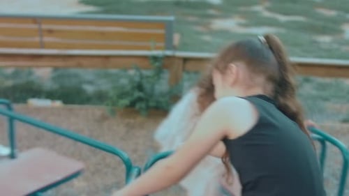 Two Cute Cheerful Little Girls are Riding on Merrygoround on Playground Having Fun on a Sunny Summer
