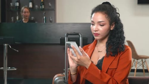 Beautiful Businesswoman with Luggage Sitting on Lounge Play Smartphone While Waiting for Boarding