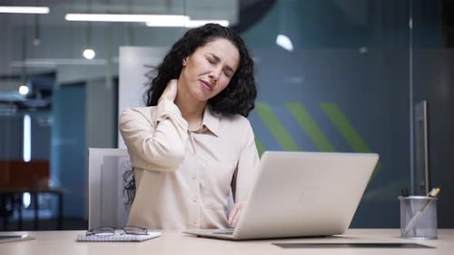 Woman Massaging Stiff Neck at Desk in Office