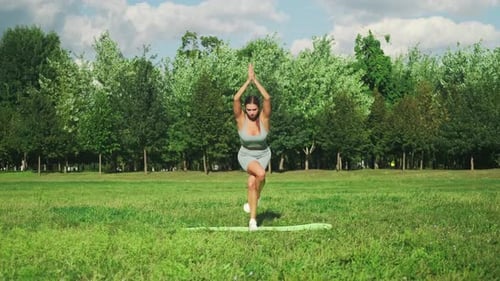 Beautiful sports girl in is engaged in stretching on a sports mat in a city park. Yoga in a sunny me
