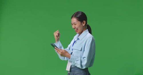Side View Of Happy Business Woman Celebrating Using Mobile Phone On Green Screen In The Studio
