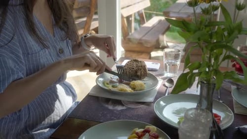 A woman eats ham for breakfast, with an omelet, vegetables, and bread.