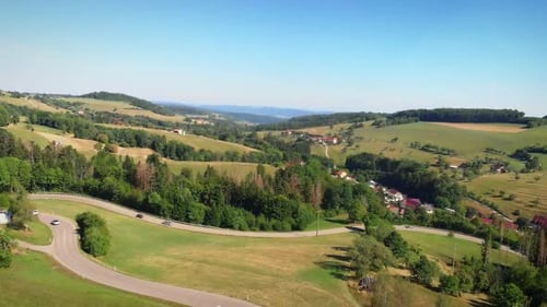Cars moving along narrow winding mountain road through green hills and meadows