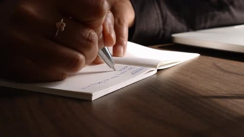 Hands Writing Notes on Desk with Laptop