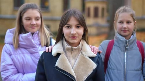 Front View Portrait of Confident Beautiful Teenage Girl Looking at Camera Smiling As Blurred Friends