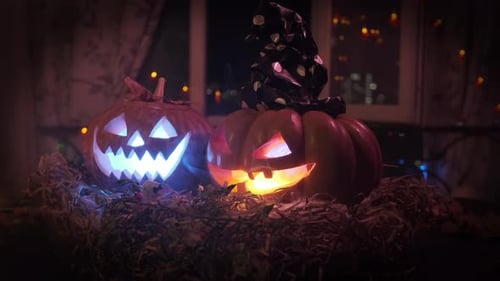 Creepy two carved Halloween pumpkins with light inside rotate in smoke lying on threshold close-up