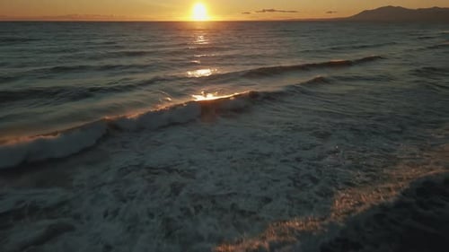 Aerial view of ocean waves tilting up into the horizon with a clear golden sky