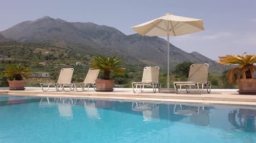 Ausblassende Kippaufnahme von Liegestühlen und Sonnenschirmen neben dem Luxuspool an sonnigen Tagen mit blauem Himmel