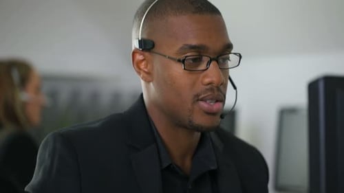 Young businessman communicating with headset typing on laptop in modern office