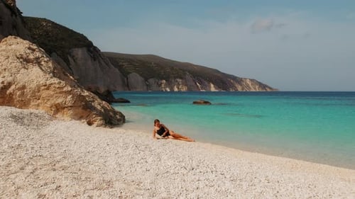 Mujer con un libro relajándose en la playa de guijarros blancos en Cefalonia junto al mar turquesa en un día soleado de verano