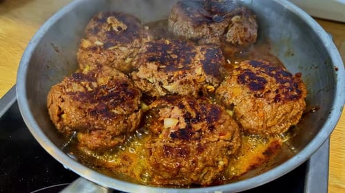 Ground beef burgers sizzling on stovetop, close up view
