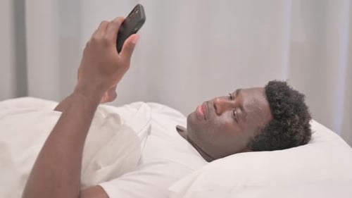 Side View of African American Man using Smartphone in Bed