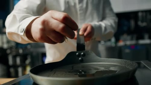professionelle Küche: Der Koch zerbricht ein Ei, um Rühreier zuzubereiten
