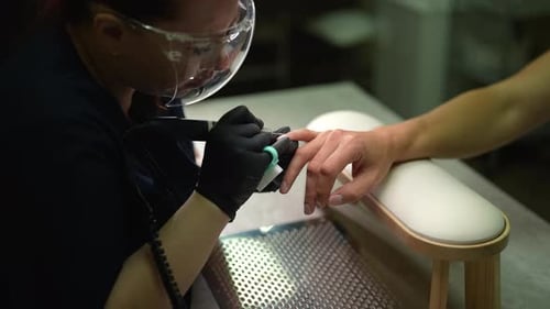 Side View of Professional Nail Technician Using Electric Nail Drill to Shape and Remove Cuticles