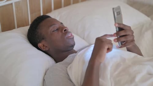 Young Adult Using Smartphone in Bed at Home