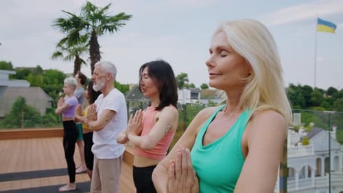 Mature Woman Practices Yoga with Multiracial Group on Terrace