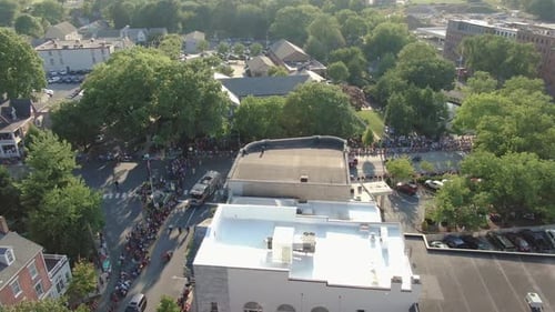 Aerial tilt down at Fourth of July parade as fire company trucks round corner, waving fans greet the
