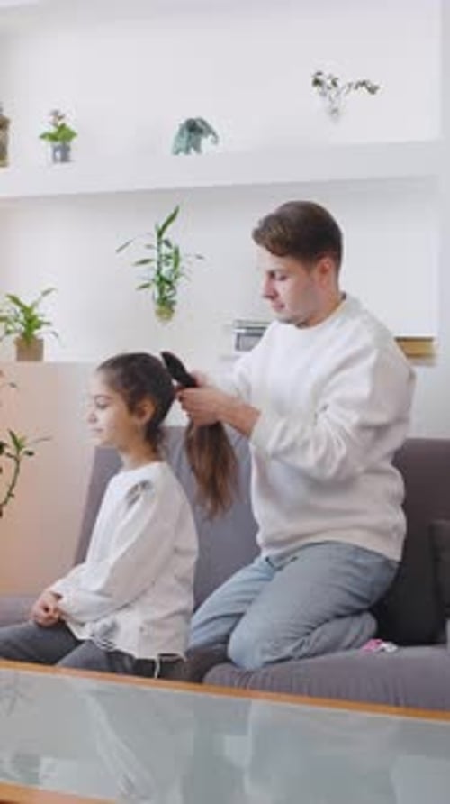 Man Combing Little Girl's Hair on Sofa at Home