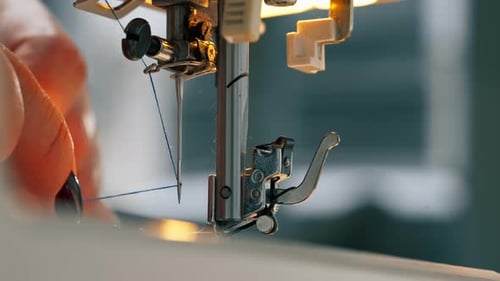 Primer plano en un taller de costura: el hilo se inserta en una aguja de una máquina
