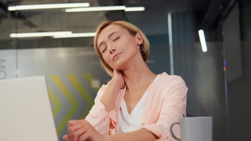 Woman Massaging Neck at Office Desk
