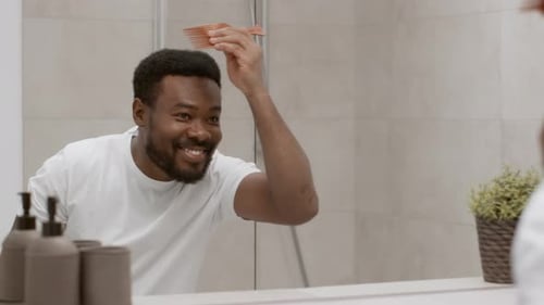 Smiling Man Combs Hair in Bathroom Mirror