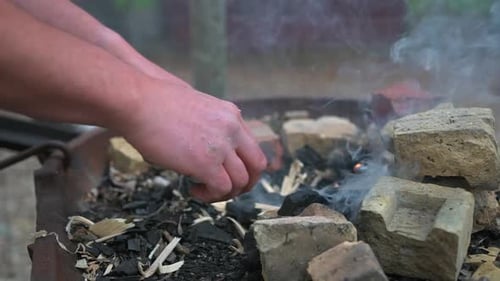 Man breaking charcoal to add to fire to forge