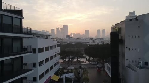 Aerial View Of Buildings In City Against Orange Sky During Foggy Weather, Drone Flying Upwards Over