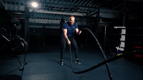 young male bodybuilder doing exercises with rope in hands in gym preparing for bodybuilding